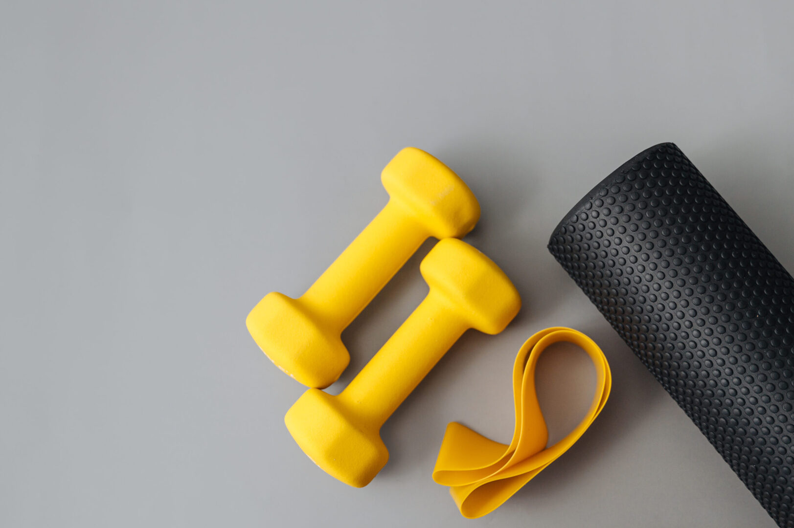 Two dumbbells, yoga mat, fitness band and thermos bottle on gray background, flat lay. Space for text